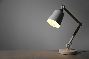 Stylish modern desk lamp on light gray table, space for text