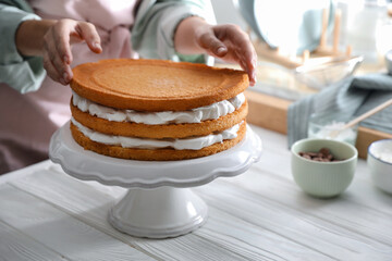 Woman stacking homemade sponge cakes at white wooden table, closeup