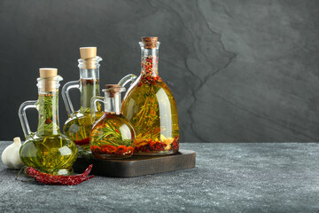 Cooking oil with different spices and herbs in jugs on light grey table. Space for text
