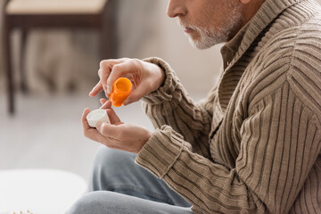 Fototapeta premium side view of cropped man suffering from parkinson disease holding pills container in trembling hands.