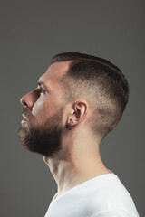 Obraz premium Male beauty concept. Profile portrait of charismatic active 30-year-old man posing over gray background. Perfect haircut. Poster style. Close up. Studio shot
