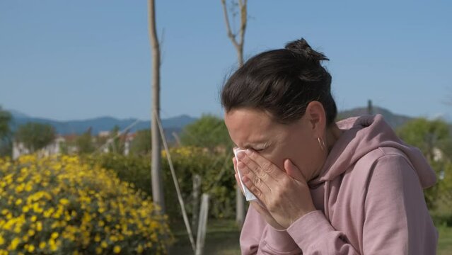 Spring rhinitis. A woman with seasonal allergies sneezes and wipes her nose with a handkerchief. Allergy to pollen.
