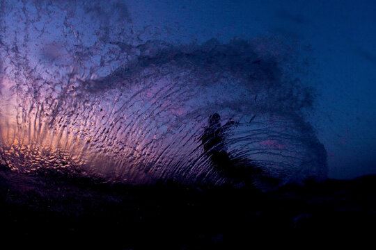 Low angle perspective of one man kiteboarding and leaving a rooster tail of spray into the sunset.