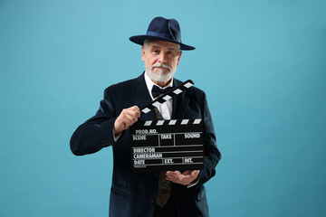 Senior actor with clapperboard on light blue background. Film industry