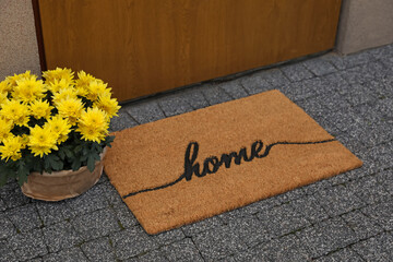 Doormat with word Home and flowers near entrance outdoors