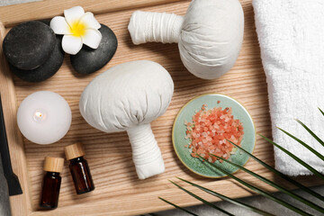 Fototapeta na wymiar Herbal massage bags, spa stones, sea salt and essential oils on grey table, flat lay