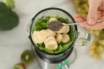 Man adding chia seeds into blender with ingredients for smoothie at table, above view