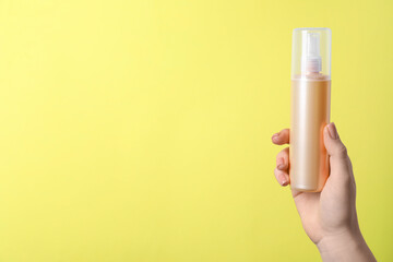 Woman holding spray bottle with hair thermal protection against pale yellow background, closeup. Space for text