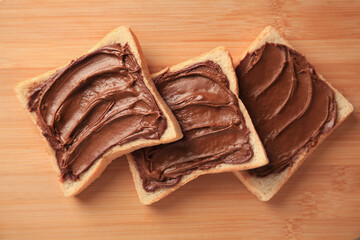 Tasty toasts with chocolate paste on wooden board, flat lay