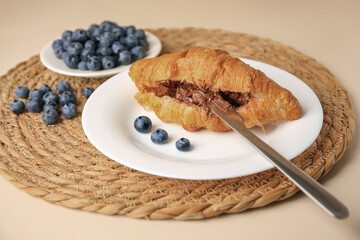 Tasty croissant with chocolate paste and blueberries on beige background
