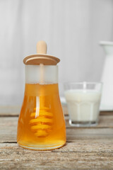 Jar with honey and glass of milk on wooden table