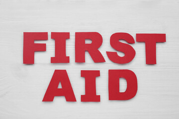 Words First Aid made of red letters on white wooden table, flat lay