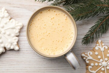 Cup of delicious eggnog, fir branch and cookies on wooden table, flat lay