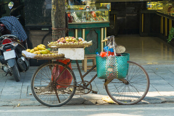 An old bike holding bags and trays of fruit parked on a sidewalk at Hanoi in Vietnam