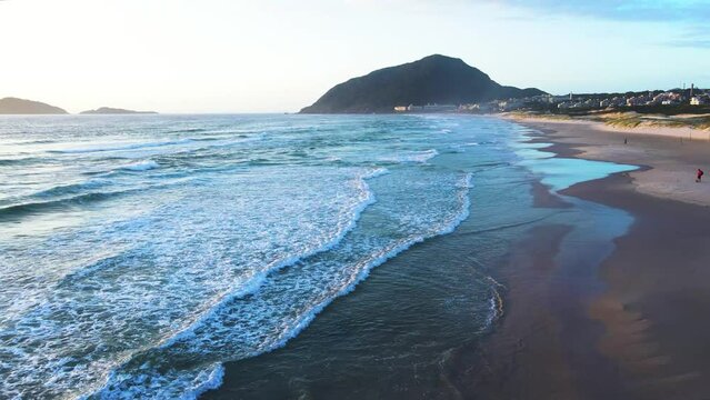 Aerial scene of a drone flying low over the sea waves on a paradisiacal beach in Florianopolis, Santinho beach with a bird passing by
