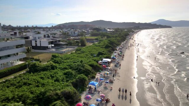 Aerial drone scene of tourist beach  with many summer houses hotels facing the sea urban beach mesh with many people enjoying the sun the sand and the sea florianopolis jurere internacional