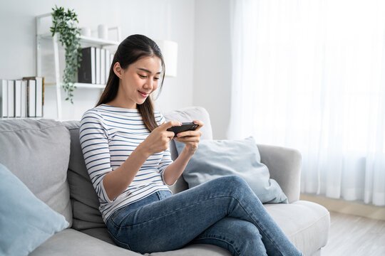 Asian young beautiful woman playing mobile game on smartphone at home. 