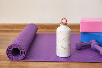 Sports water bottle with equipment on mat near light wall