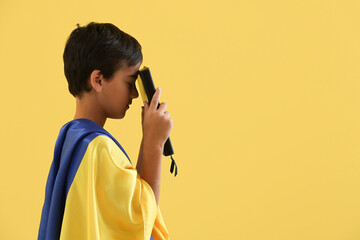 Little boy with Holy Bible and flag of Ukraine praying on yellow background