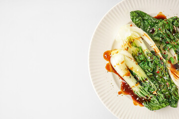 Plate of tasty stewed pak choi cabbage with soy sauce on white background, closeup