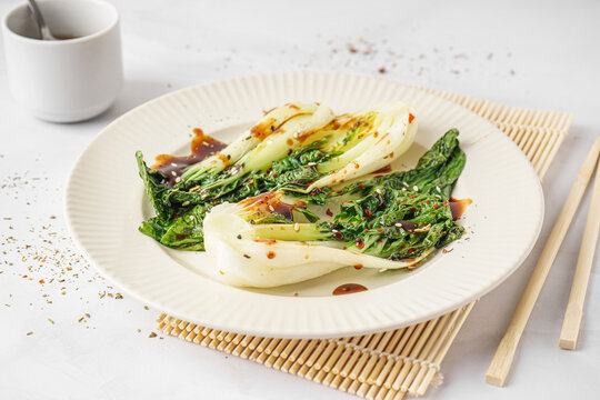 Plate of tasty stewed pak choi cabbage with soy sauce on light background