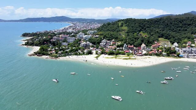 Aerial drone scene of paradise beach with many boats and yachts in the sea with pier and buildings facing the sea in Canajure beach Florianopolis Santa Catarina