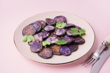 Plate with slices of fried purple potatoes and cilantro on color background