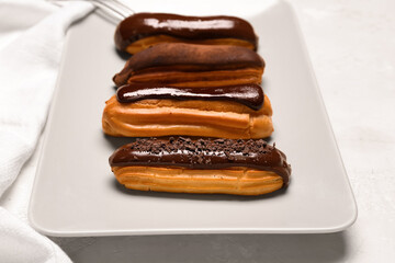 Plate with sweet chocolate eclairs on light background, closeup