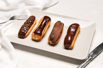 Plate of sweet chocolate eclairs on light background