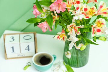 Vase with beautiful alstroemeria flowers, cup of coffee and cube calendar on table near color wall, closeup.  Mother's day celebration