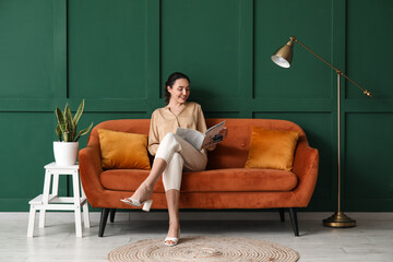 Young woman reading magazine on red sofa near green wall - Powered by Adobe