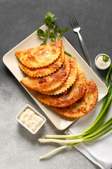 Plate with tasty chebureks, parsley, onion, sauce and fork on grunge background
