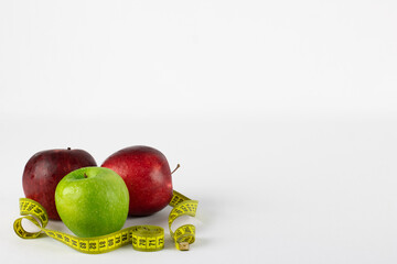 Red and green apples in rolled up on a measuring tape, symbolizing healthy life, on white background