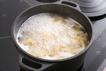 Cooking pot with boiling pasta on electric stove, closeup