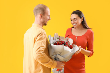 Young man greeting his wife with bouquet of flowers on yellow background. Valentine's Day celebration