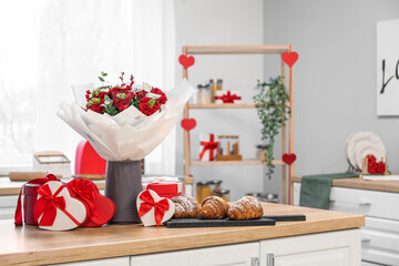 Vase with flowers, croissants and gifts for Valentine's Day on counter in kitchen