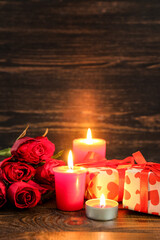 Burning candles, gift boxes and rose flowers on wooden background. Valentine's Day celebration