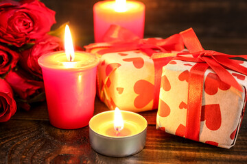 Burning candles and gift boxes on wooden background, closeup. Valentine's Day celebration