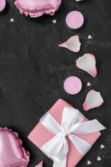 Composition with gift box, candles and rose petals on dark background, closeup. Valentine's Day celebration