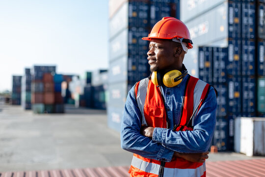 Black male African American smiling engineering in uniform wear hard hat standing containers yard. Area logistics import export and shipping.