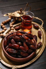 Tray with dates, glass of tea, prayer beads and Muslim lamp for Ramadan on dark wooden background, closeup