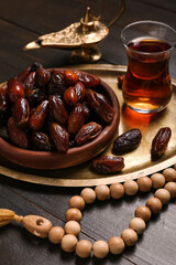 Tray with dates, glass of tea, prayer beads and Muslim lamp for Ramadan on dark wooden background, closeup