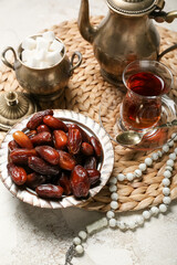 Mat with dates, glass of tea, sugar and prayer beads for Ramadan on grunge background