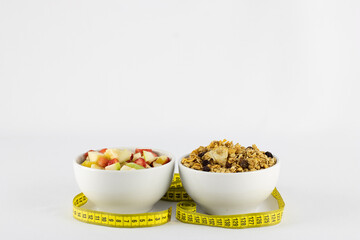 Chopped tropical and juicy fruits, granola, rolled up in measuring tape, symbolizing healthy life, on white background