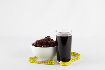 Glass of grape juice accompanied by a bowl of fresh and cold grapes on white background