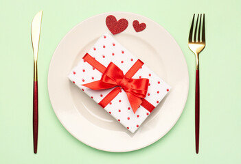Table setting with gift box and hearts on green background. Valentine's Day celebration