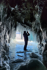A man is hiking in a beautiful ice cave. A man traveling in winter, standing on a frozen lake with an ice cave. A man explores an amazing glacier cave . Selective focus. 