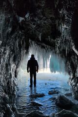 A man is hiking in a beautiful ice cave. A man traveling in winter, standing on a frozen lake with an ice cave. A man explores an amazing glacier cave . Selective focus. 