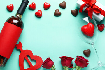 Frame made of wine bottle, chocolate candies and rose flowers on turquoise background. Valentine's Day celebration