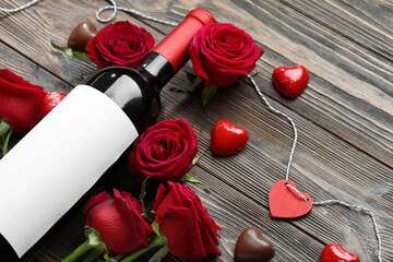 Bottle of wine, chocolate candies and rose flowers on wooden background. Valentine's Day celebration